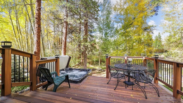 Una terraza de madera con un jacuzzi, una mesa con sillas y una barandilla.