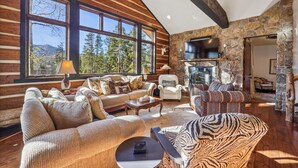 L’intérieur d’une cabane en rondins, avec une cheminée en pierre, de grandes fenêtres et un coin salon confortable.
