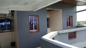 Edifício residencial com duas janelas adornadas por grades de metal decorativas, piso de azulejos e varanda de concreto.