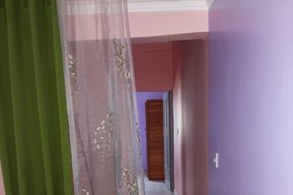 A hallway with a wooden door at the end, a purple wall, and a green curtain partially drawn.