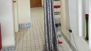 Un pasillo con suelo de baldosas, una puerta de madera y una cortina.