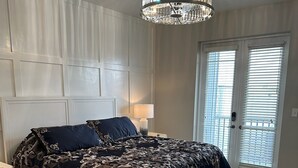 Un dormitorio con una cama grande, una araña, una mesita de noche y una puerta con persianas.