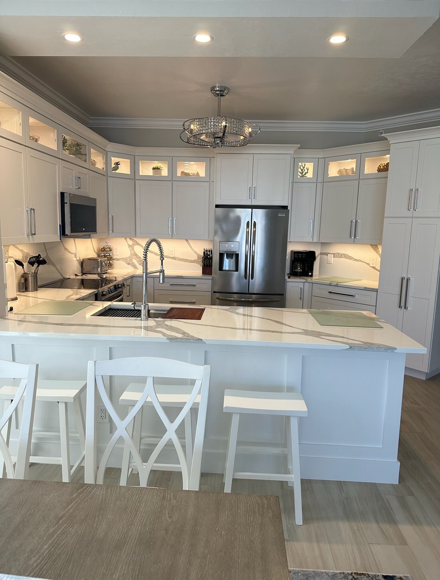 A modern kitchen with white cabinetry, a stainless steel refrigerator, a built-in oven, and a marble countertop.
