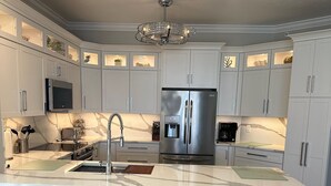 Una cocina moderna con armarios blancos, un refrigerador de acero inoxidable, horno empotrado y encimera de mármol.