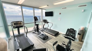 Gimnasio con cintas de correr, bicicleta estática y máquina de remo, con vistas a la playa.