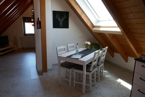 A dining area with a white table and chairs, a black framed picture on the wall, and a skylight above.