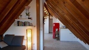 Ein Dachzimmer mit einer Couch, einer Stehlampe, einem Bücherregal und einem roten Kühlschrank.