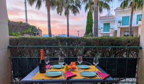 A table set for two with plates, cutlery, and a bottle of wine, overlooking a scenic view with palm trees and a building in the background.