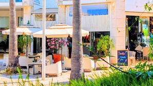 Een café met terras, palmbomen en een bord waarop ontbijtopties staan.