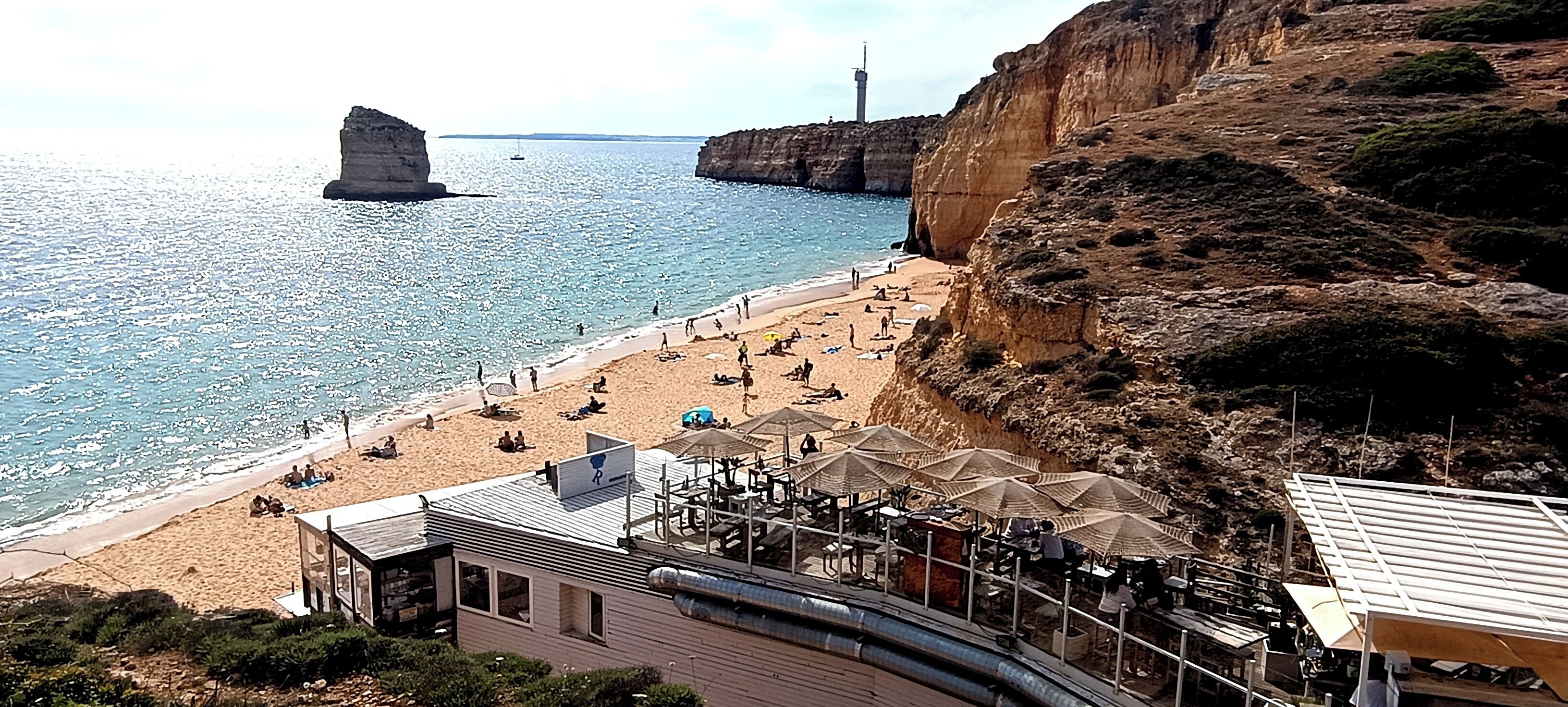 Una playa con sombrillas, un edificio de techo inclinado y acantilados rocosos.