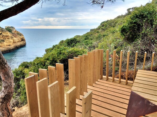 A wooden staircase leading down to a beach with a view of the sea and cliffs.