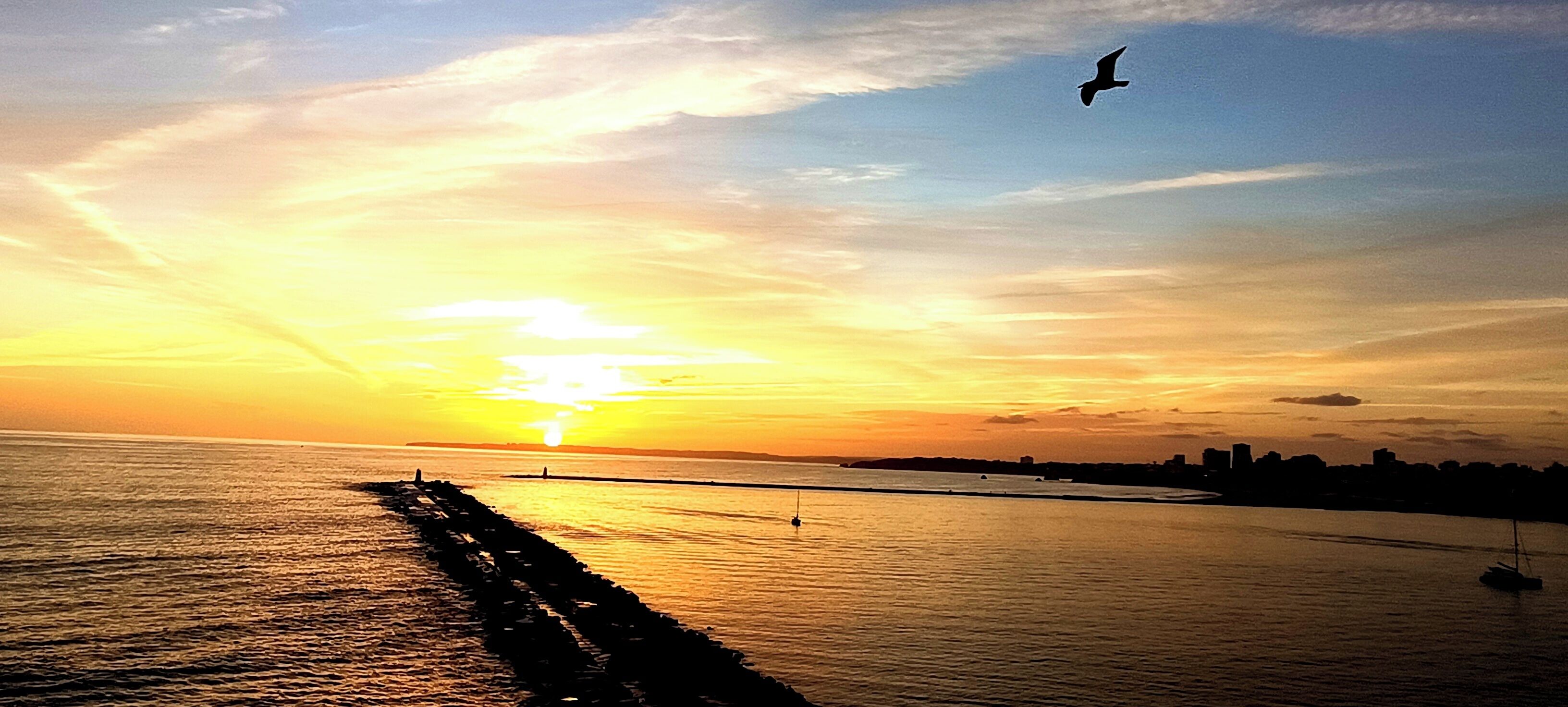 A sunset over a calm body of water with a pier extending into the water.