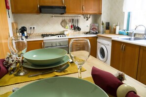 A kitchen with wooden cabinets, a stove, and a sink. There are green plates, a wine glass, and a yellow placemat on the table.