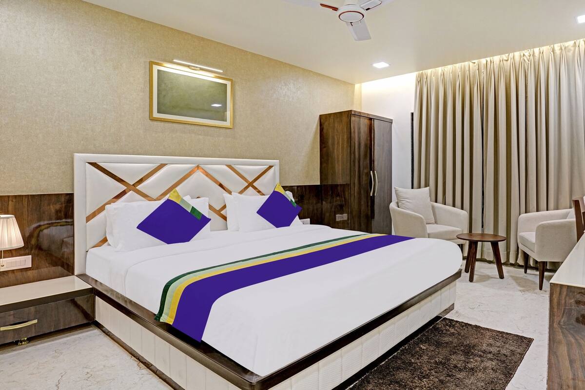 A hotel room with a large bed, a desk, a chair, a wardrobe, and a ceiling fan.