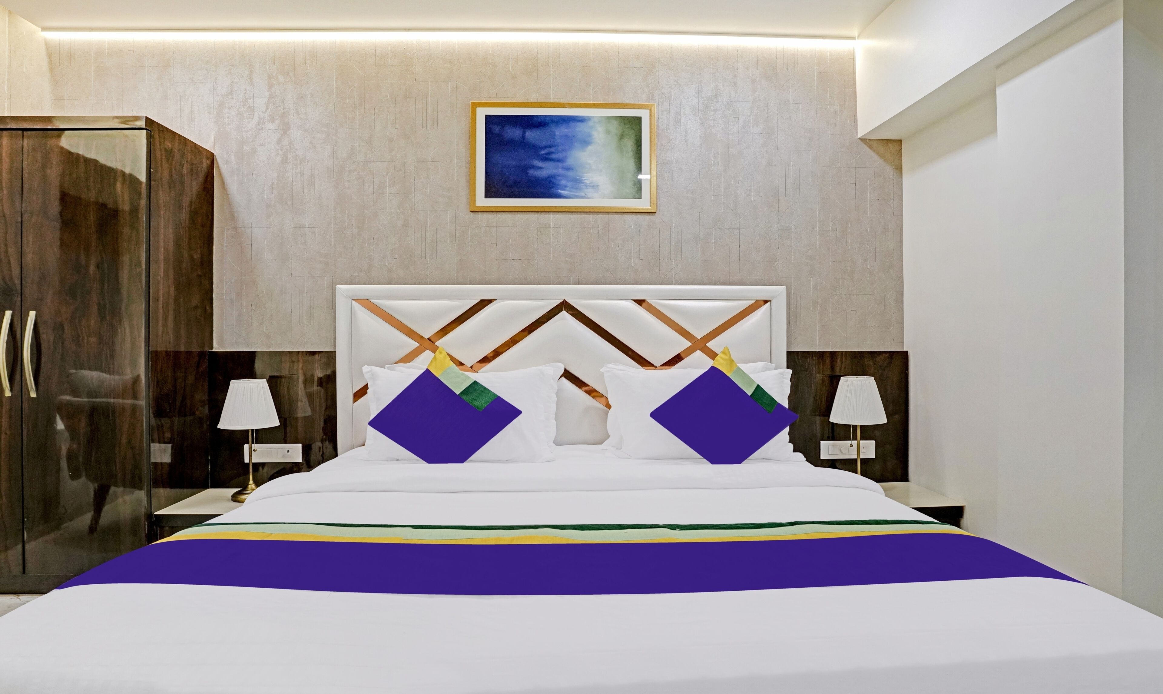 A modern hotel room with a large bed, a wooden wardrobe, and a painting on the wall.