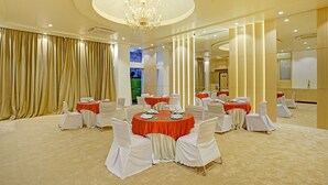 Une salle de banquet avec des tables rondes, des chaises blanches et un lustre.