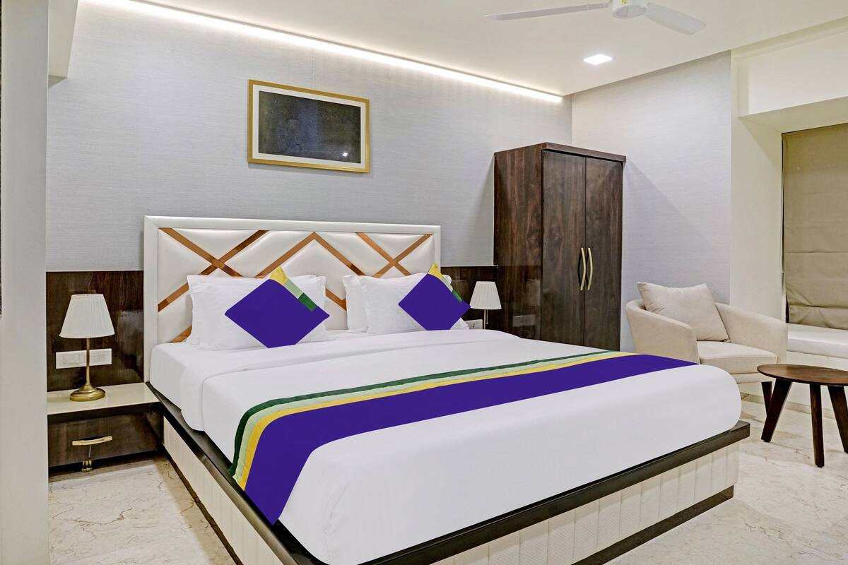 A modern hotel room with a large bed, a wardrobe, a seating area, and a ceiling fan.