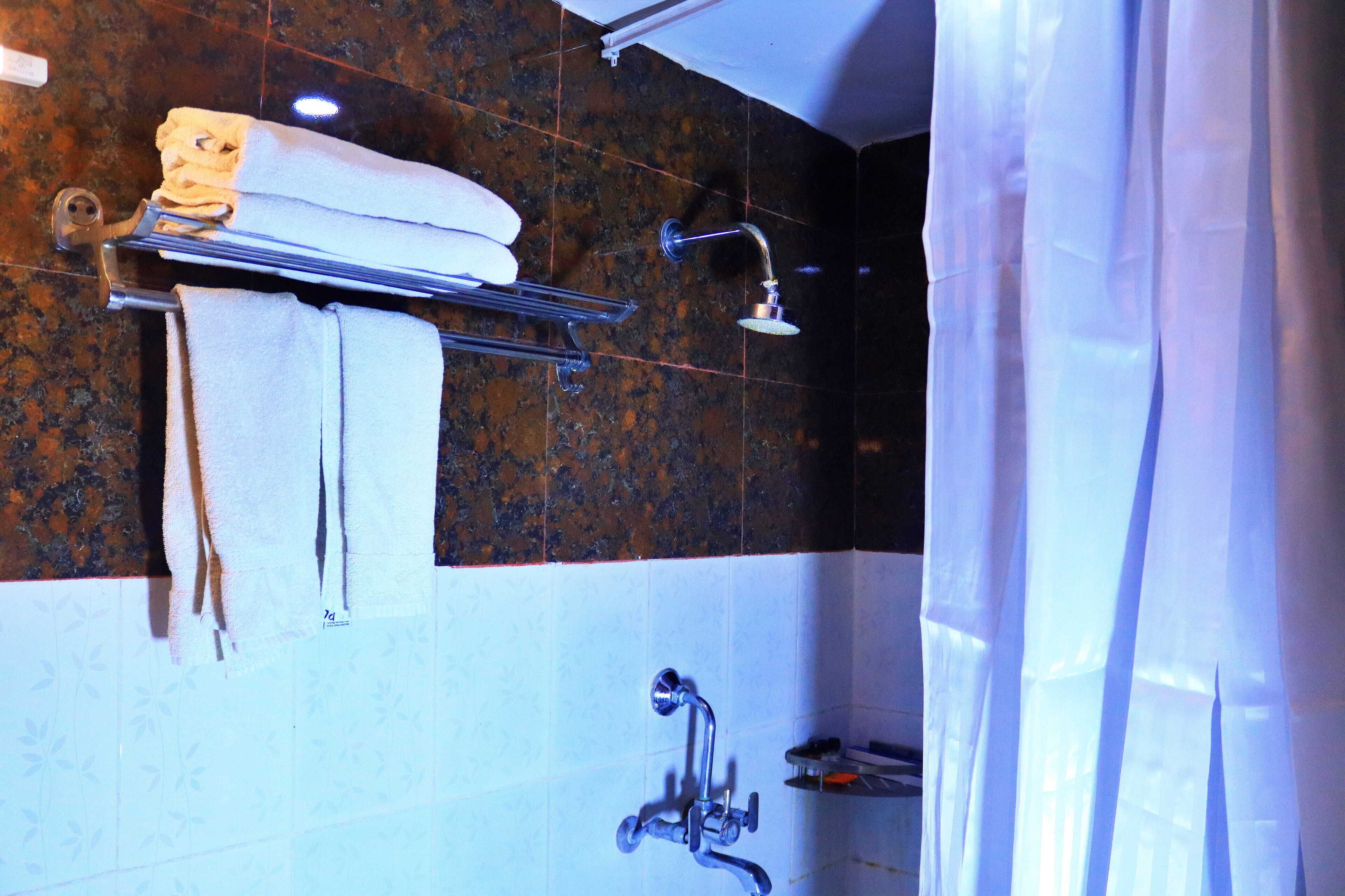 A bathroom with a shower, a towel rack with towels, and a tiled wall.