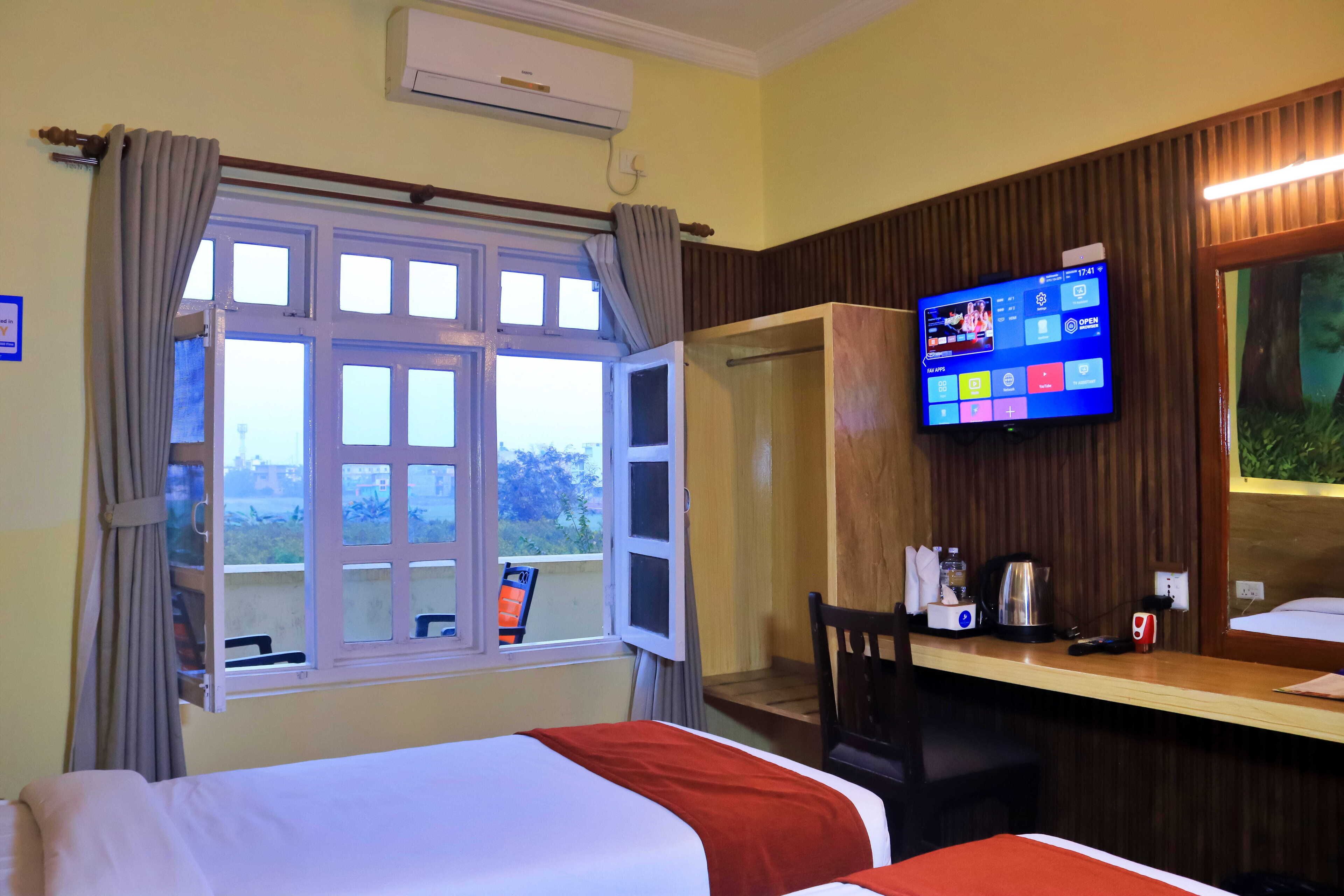 A hotel room with a bed, a desk with a computer, a shower, and a window with curtains.