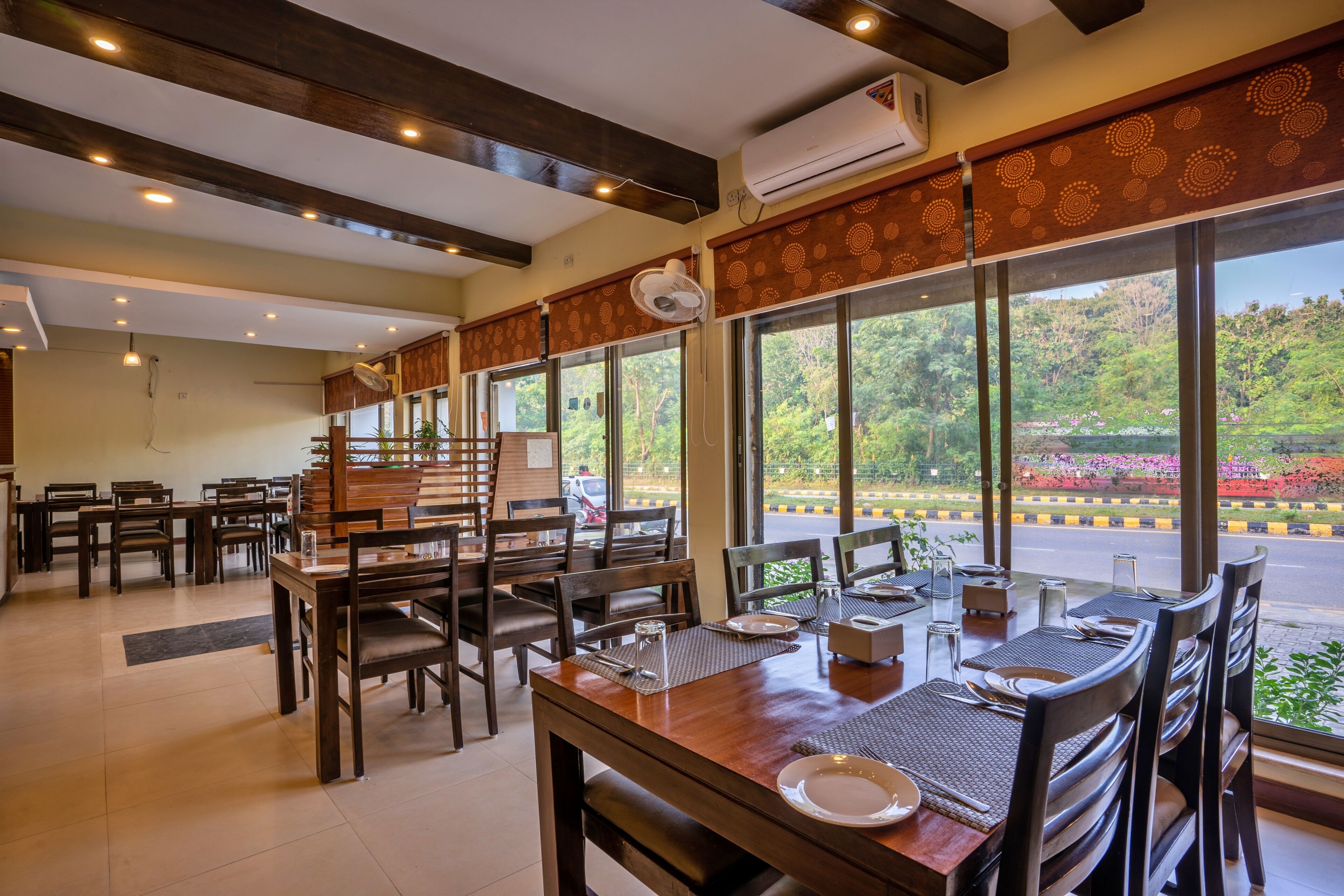 A restaurant with wooden furniture and large windows offering a view of greenery.