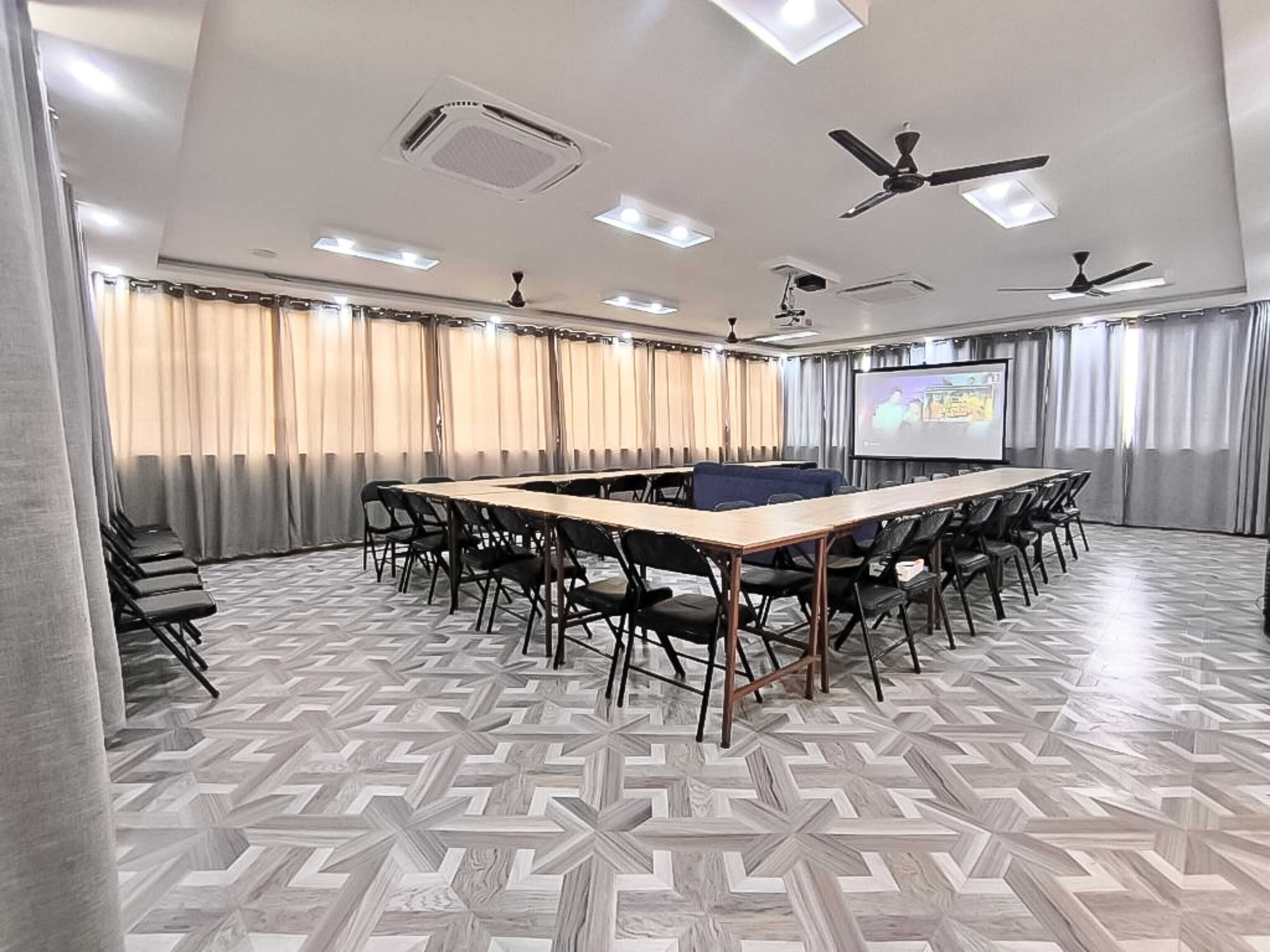 A conference room with a long table, chairs, a projector screen, and ceiling fans.