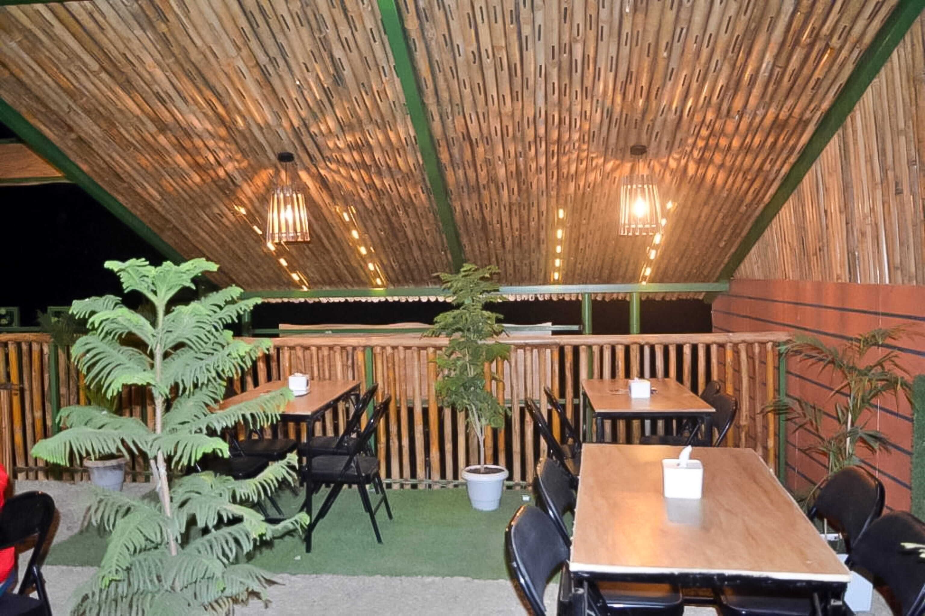 An outdoor dining area with bamboo walls, tables, chairs, and hanging lights.