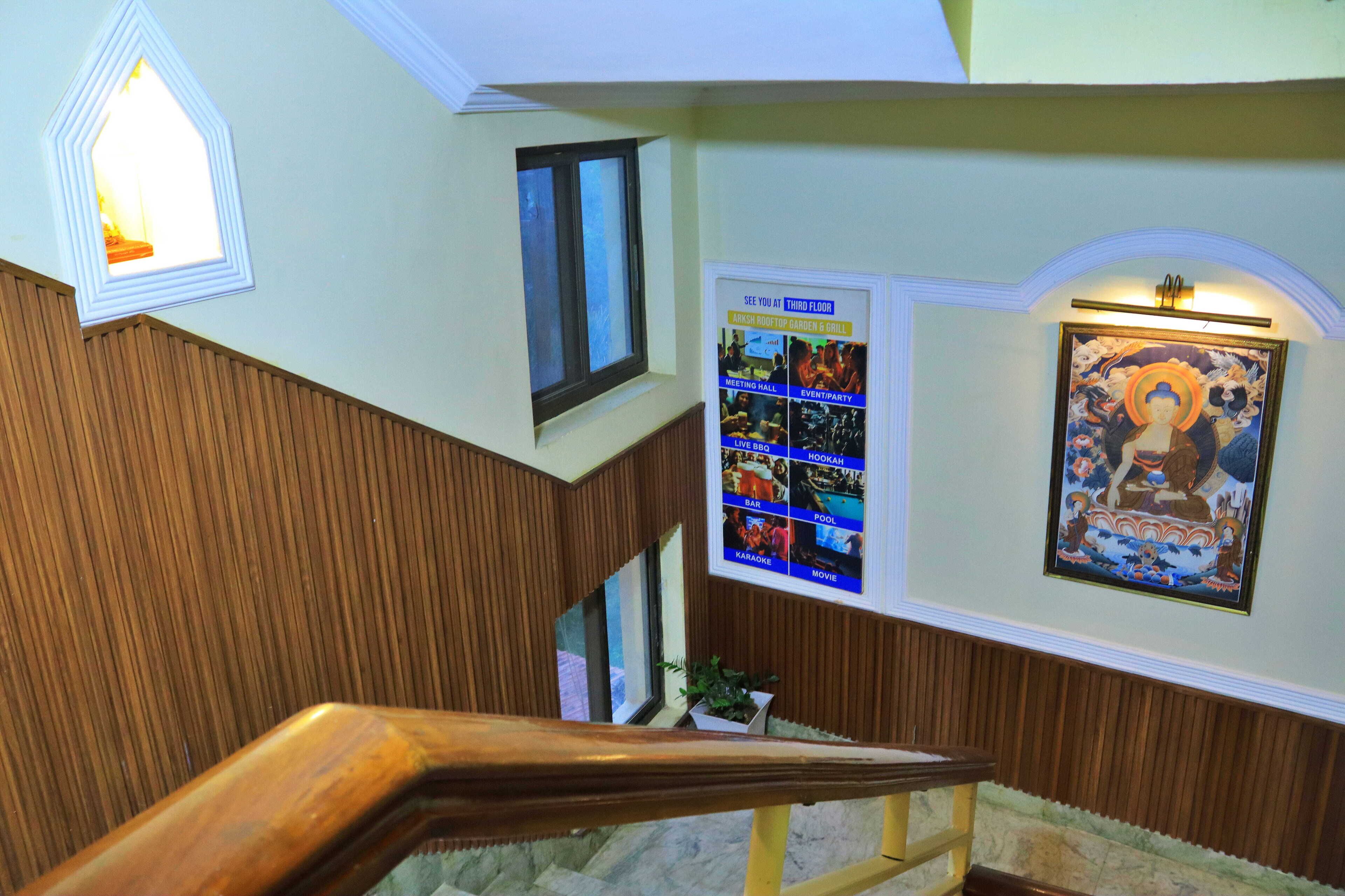 Una escalera con barandillas de madera, un tablón de anuncios con carteles de eventos y una obra de arte enmarcada en la pared.