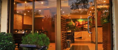 Un restaurante con entrada de vidrio, mesas al aire libre y vista a la calle.