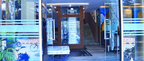 A modern interior with a glass door entrance, a wooden reception desk, and a view through the glass to the outside.