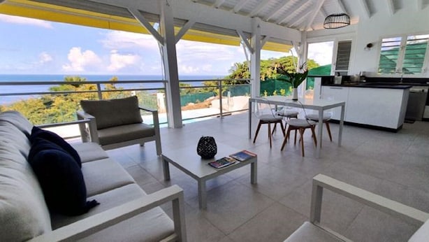 Uma sala de estar moderna com sofá, mesa de centro e cadeiras, uma cozinha equipada e vista para o oceano.