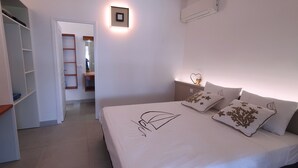 Um quarto com cama, mesas de cabeceira, escrivaninha, guarda-roupa e espelho.