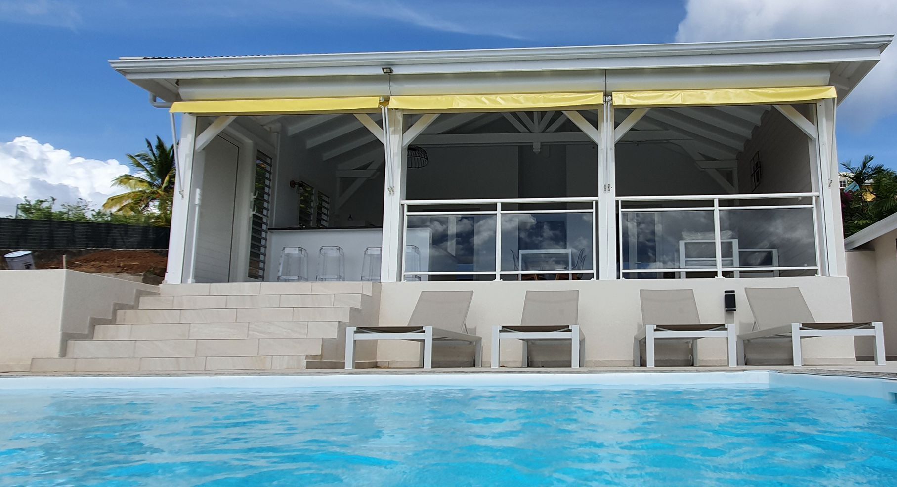 A modern house with a pool, featuring a covered patio with chairs and a staircase leading to the entrance.