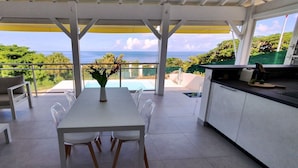 Uma área de refeições ao ar livre com vista para o oceano, uma piscina e um terraço coberto.