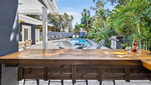 A wooden bar with a pool and lounge chairs in the background. - Steps to beach/Tiki Bar/Heated Pool/fun! (Indian Rocks Beach)