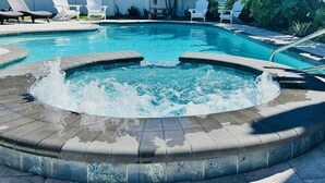 A swimming pool with a hot tub in the center, surrounded by lounge chairs and a patio area. - Steps to beach/Tiki Bar/Heated Pool/fun! (Indian Rocks Beach)