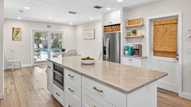 A modern kitchen with white cabinetry, a large island, stainless steel appliances, and a view to an outdoor patio. - Steps to beach/Tiki Bar/Heated Pool/fun! (Indian Rocks Beach)