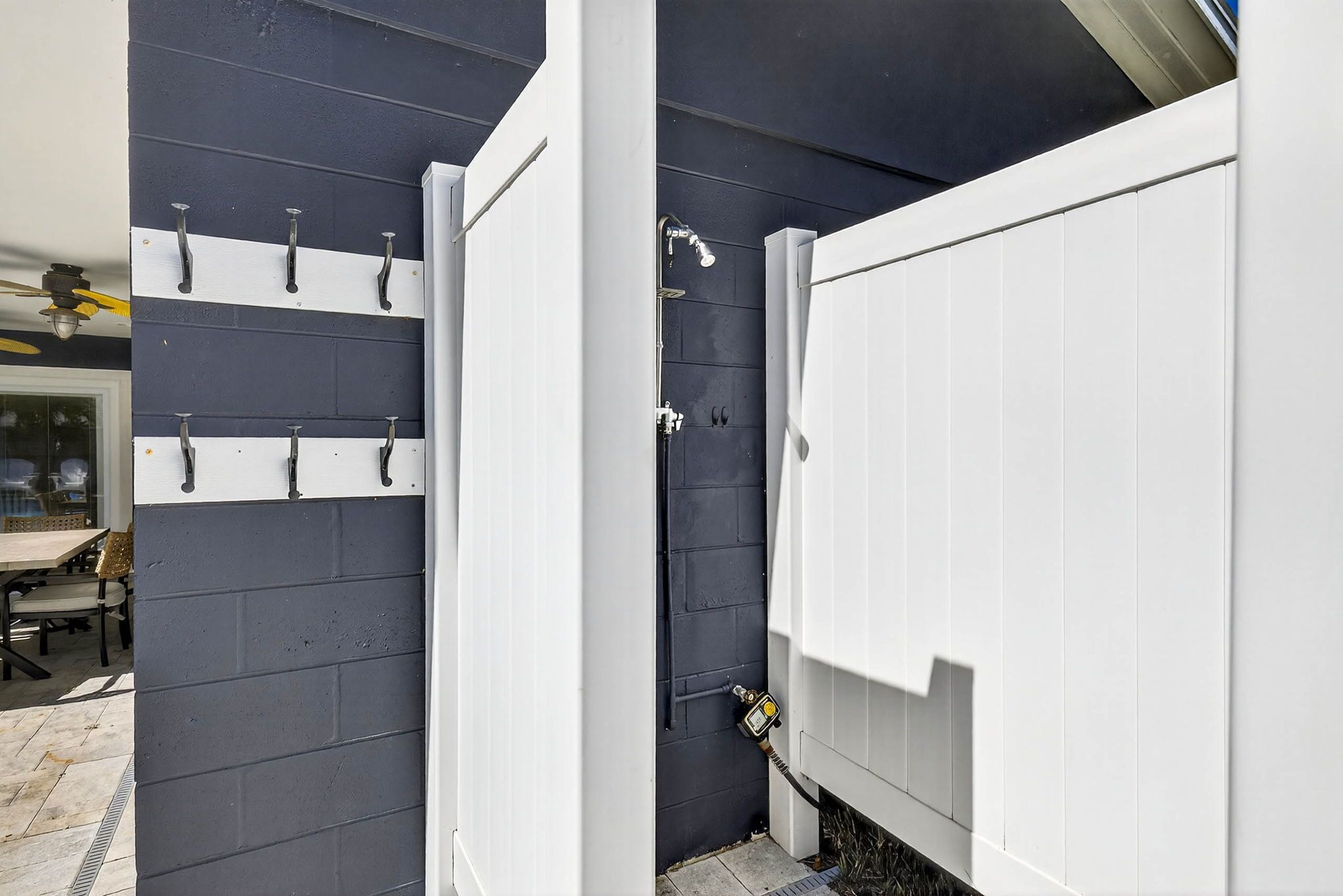 Un espace de douche extérieur moderne, doté d’une porte blanche, d’un pommeau de douche en métal et d’un tuyau fixé au mur.