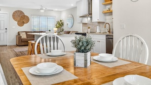 A modern kitchen with white cabinets, a stainless steel range hood, and a dining area with a wooden table set for four. - Steps to beach/Tiki Bar/Heated Pool/fun! (Indian Rocks Beach)