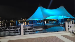 Vista nocturna de una zona ribereña con una gran estructura iluminada en azul, una entrada con puerta y un camino pavimentado.