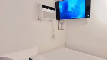 Une chambre avec un lit, un climatiseur fixé au mur et un téléviseur à écran plat affichant une image bleue.