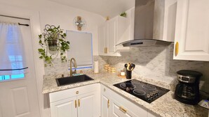 Una cocina moderna con armarios blancos, un lavamanos negro, una campana extractora de acero inoxidable y una cafetera.