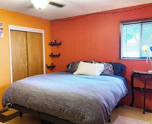 Cozy retreat with a single bed, wooden door, and window with blinds, plus a convenient table nearby.
