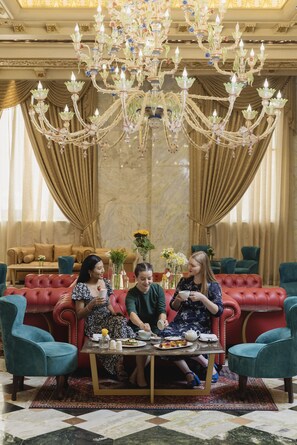 A luxurious room with a red sofa, teal chairs, and a chandelier. - Dusit Hotel & Suites Doha (Doha)