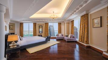 A spacious hotel room with a large bed, a sitting area with sofas, a chandelier, and large windows offering a city view.