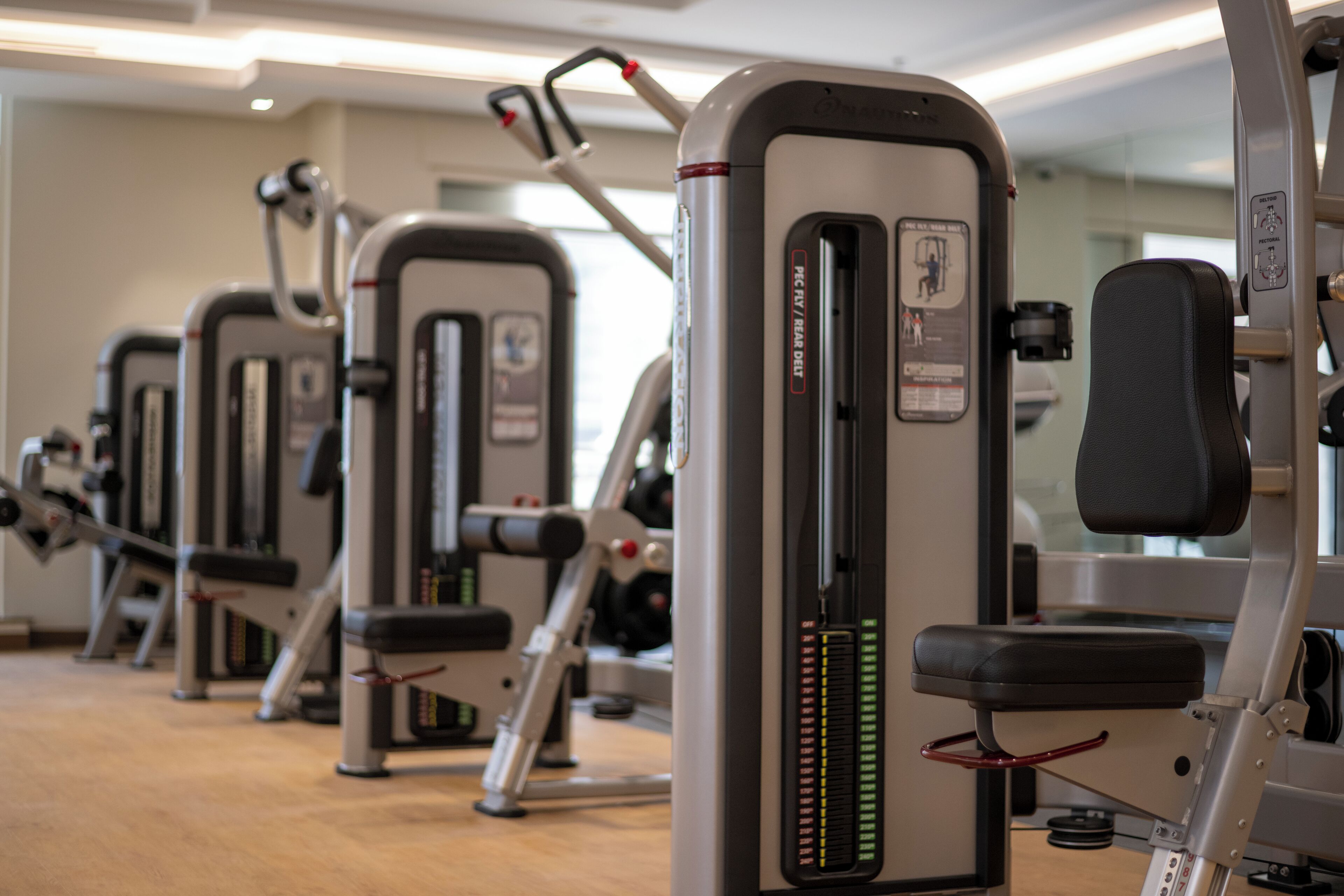 A row of stationary exercise machines in a gym with a wooden floor.