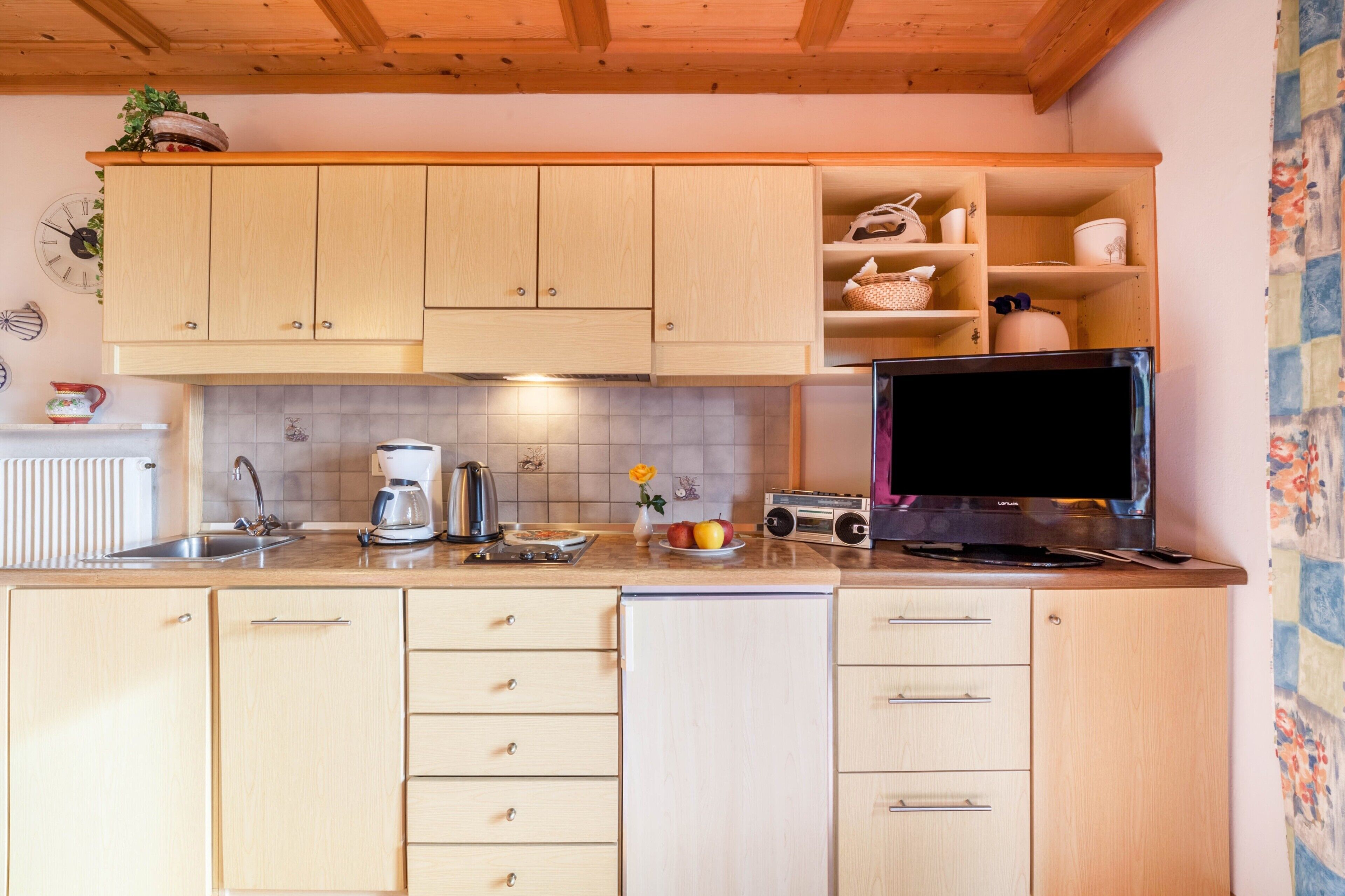 Une cuisine avec des meubles de rangement en bois, une machine à café, un grille-pain et une radio.