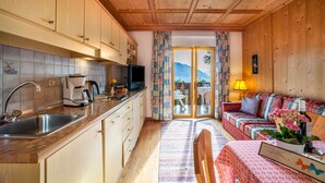 Eine Küche mit Spüle, Herd und Schränken, ein Essbereich mit Tisch und Stühlen sowie ein Wohnzimmer mit Sofa und Fernseher.