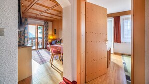 Ein Zimmer mit Holzbalkendecke, einem Essbereich mit Tisch und Stühlen sowie Blick durch eine Tür.