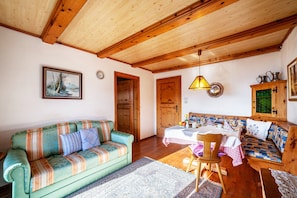 Una sala de estar acogedora con un sofá, una mesa de comedor y un banco. El techo es de madera y hay un cuadro en la pared.