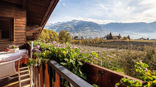 Un balcón de madera con una mesa y sillas, con vistas a un viñedo y montañas.